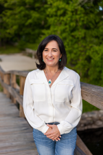 Author Jennifer Crystal wearing a white blouse and blue jeans, she has dark shoulder length hair and