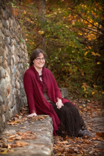 A woman sitting in front of a stone wall wearing a red sweater
