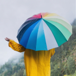 A photo with person with a yellow raincoat and rainbow umbrella holding their hand out to check the 