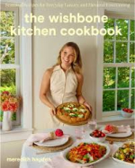 blonde woman standing in a kitchen .  in front of her is a table covered with serving dishes of food