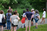 various people listen to someone talking in front of some plants.