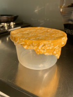 A clear bowl sits on a counter, wrapped in beeswax wrap. The beeswax wrap is a yellow fabric and wra