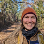 Jessie James wearing a hat with fall foliage in the background.