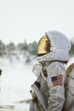 A person in a space suit with and American Flag on the arm looks up in a snowing field.