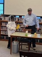 A young person in a beekeepers white hat, gloves and chirt stand next to an older man.