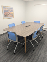 Gray rectangular table with six blue chairs in a rectangular room.