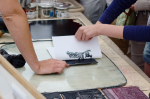 An image of two people making a paper print with linocut materials.