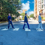 Three white men holding books cross a Boston street in an inimitation of the Beatles on Abbey Road