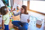 A child with a parent pointing to a smiling face on paper.