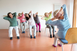 A group of ladies sitting in chairs doing a yoga stretch.