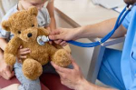 A stuffed teddy bear having his heart listened to by a doctor.
