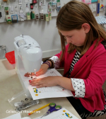 A young girl sitting at a sewing machine.