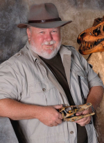 Older white male paleontologist posing in archeological gear  and hat while holding a fossil in his 