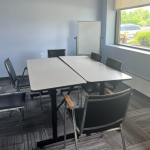 Six chairs arranged around two long tables pushed together with a whiteboard in the back of the room