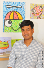 A man wearing a collared shirt smiles at the camera. Behind him are colorful, cartoon-like paintings