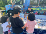 kids drawing on a table in front of a bus.