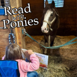 child reading picture book to pony in a stable