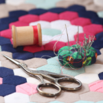 Stork scissors, needles, and a spool of thread resting on a quilt project.