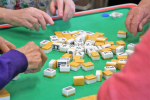Mahjong tiles in the center of the table with players' hands reaching in.
