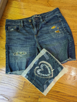Blue jean shorts have been repaired with decorative colorful stitching.