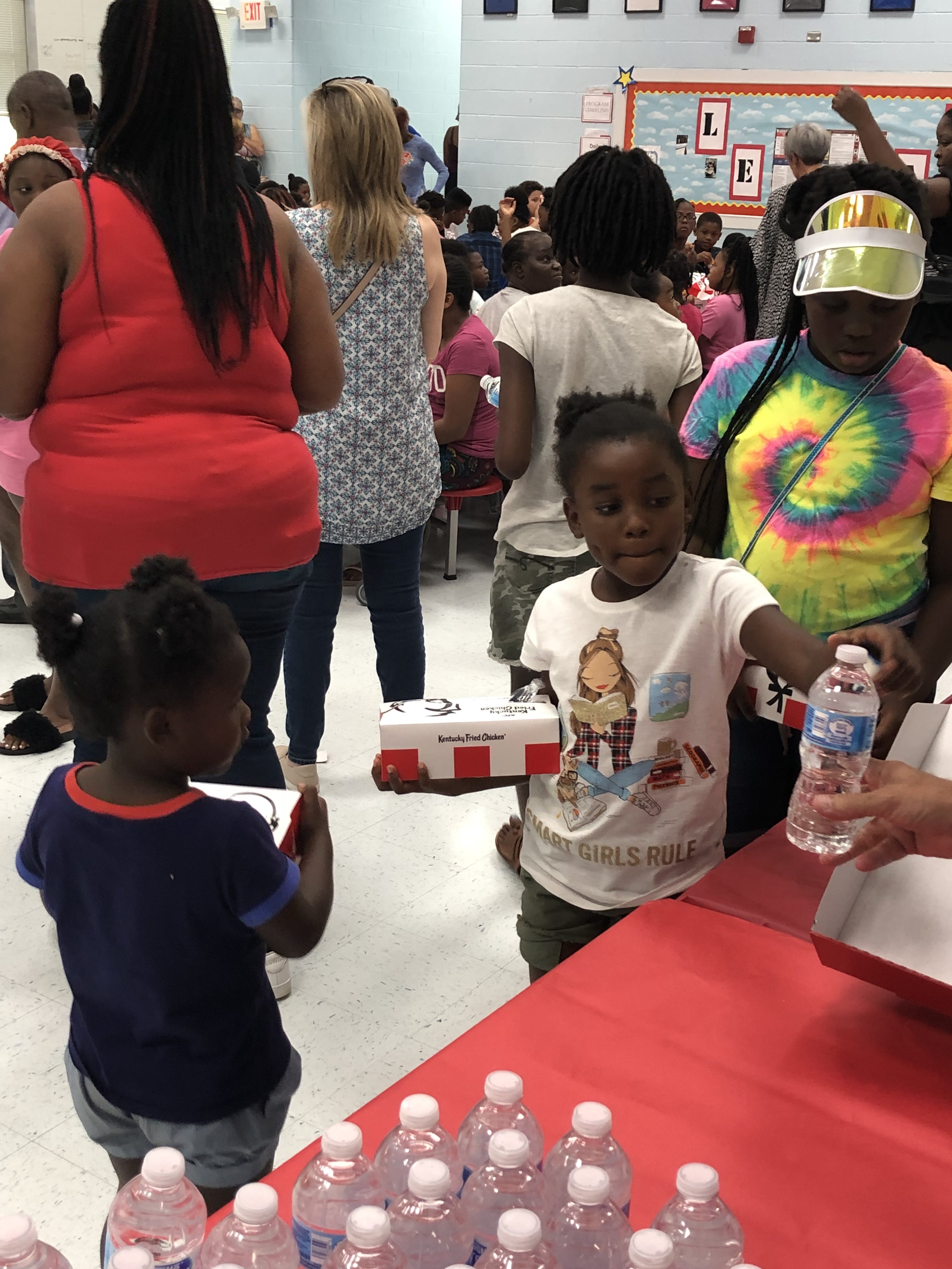 A girl wearing a "Smart girls rule" graphic tee grabbing a water bottle from a volunteer.