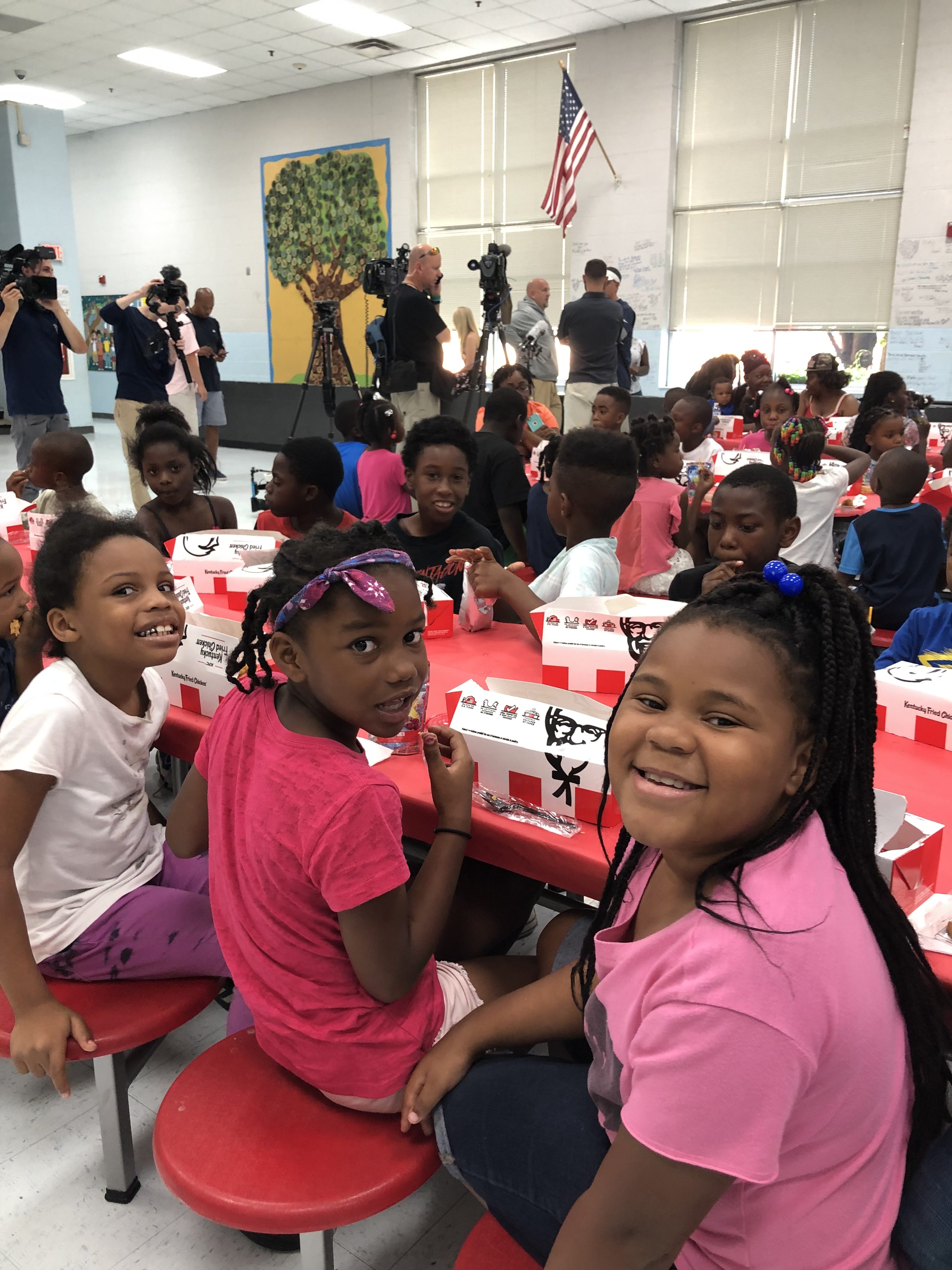 Three young girls wearing pink eating KFC food at a cafeteria table