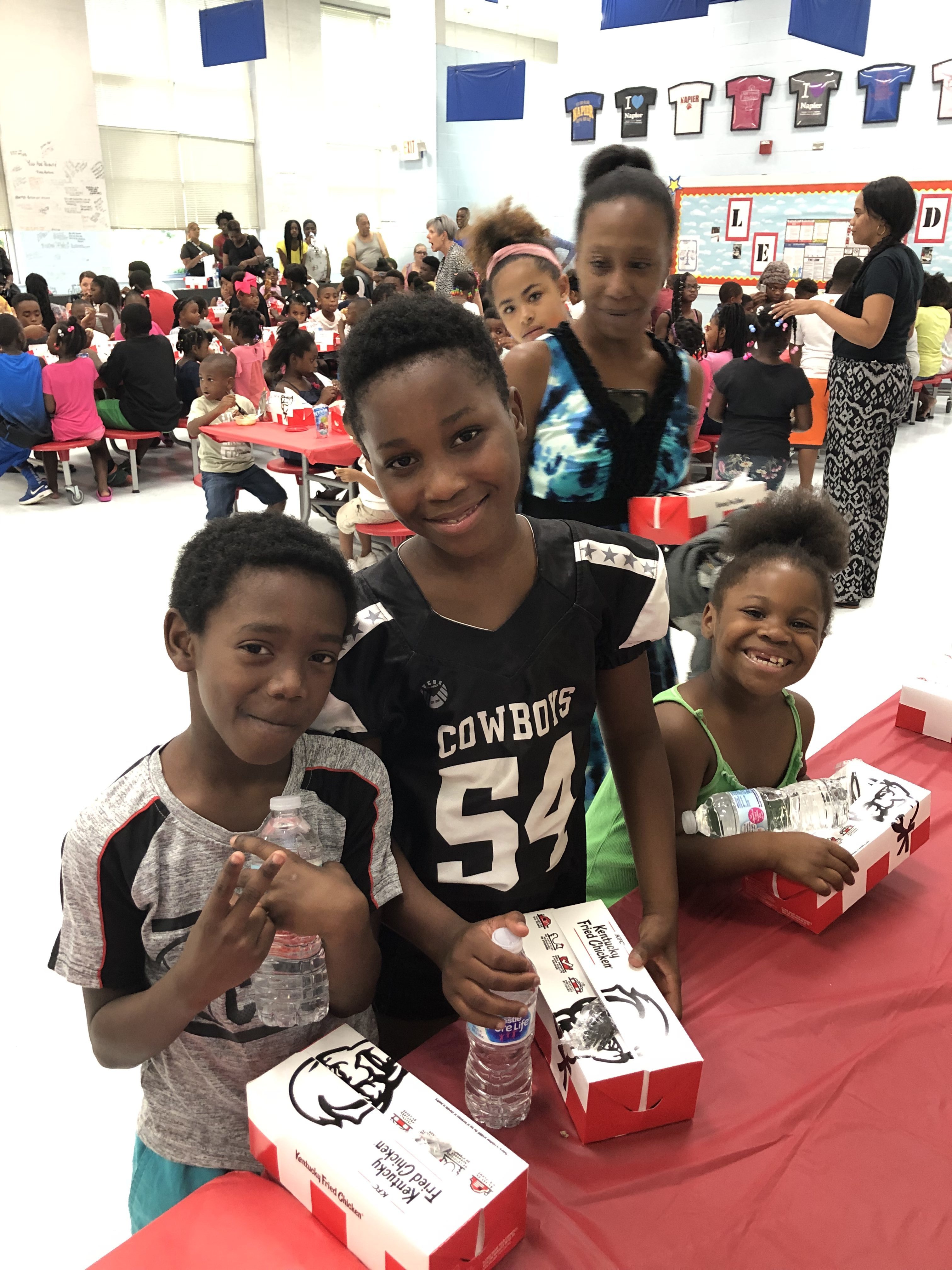 A young boy with two sisters holding KFC boxes and smiling at the camera.