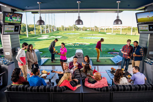Colleagues gathered in a Topgolf hitting bay with food and drinks