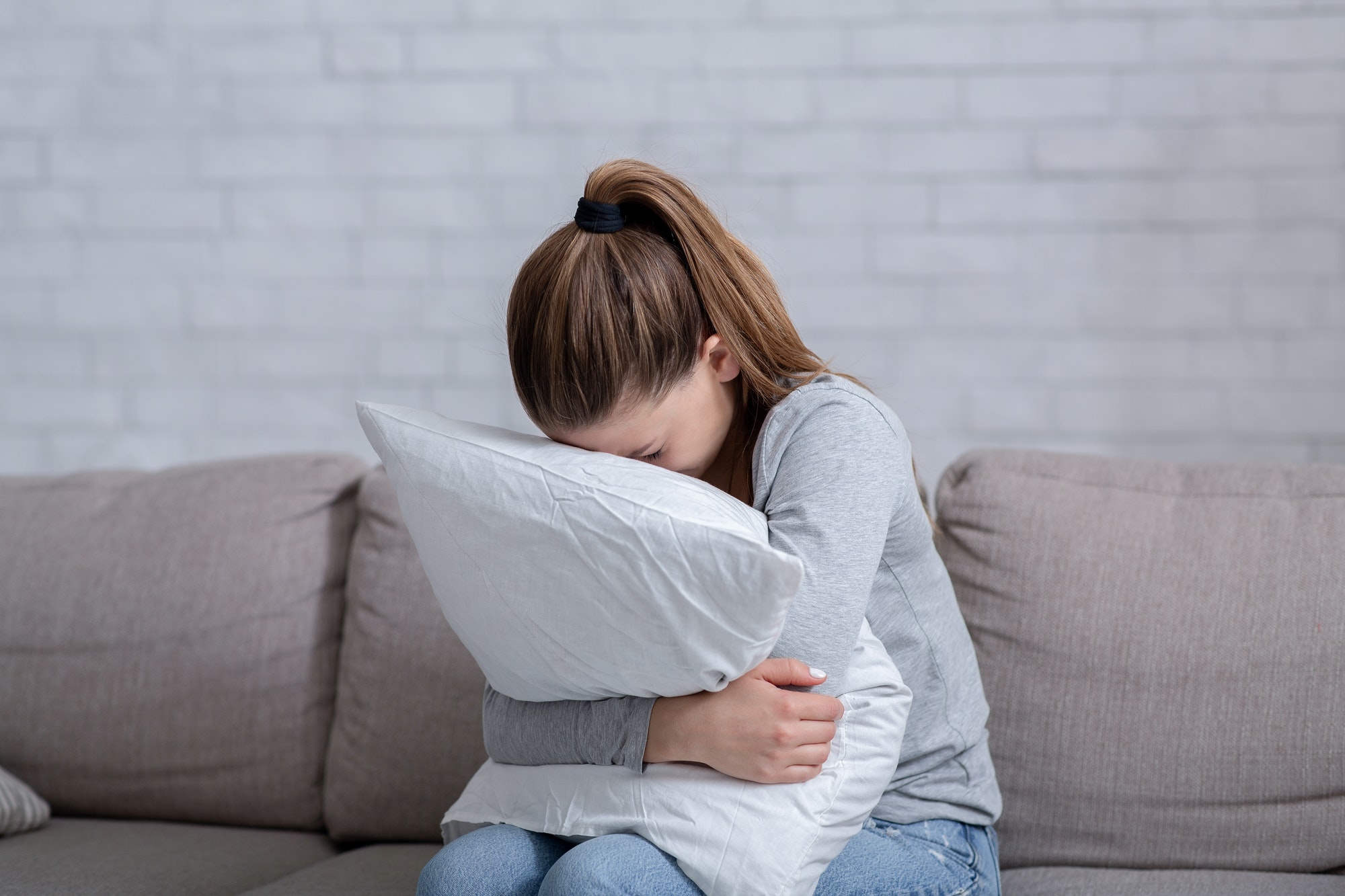 Young woman with depression hugging pillow and crying on sofa at home
