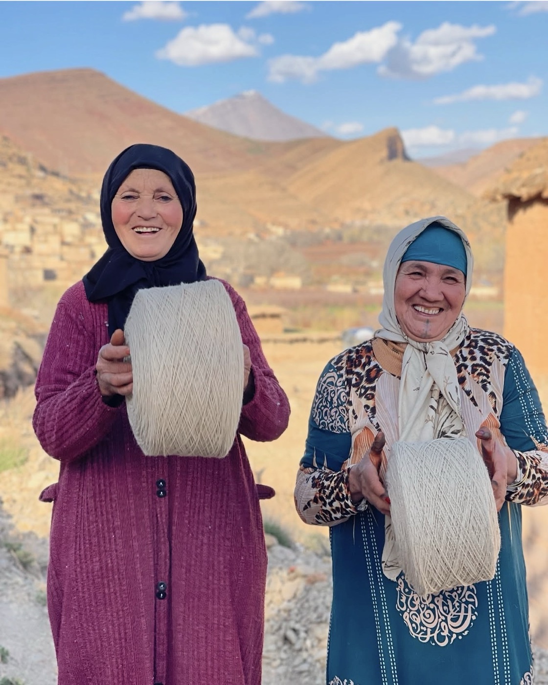 Two artisans smiling and holding cones of undyed wool yarn in their village