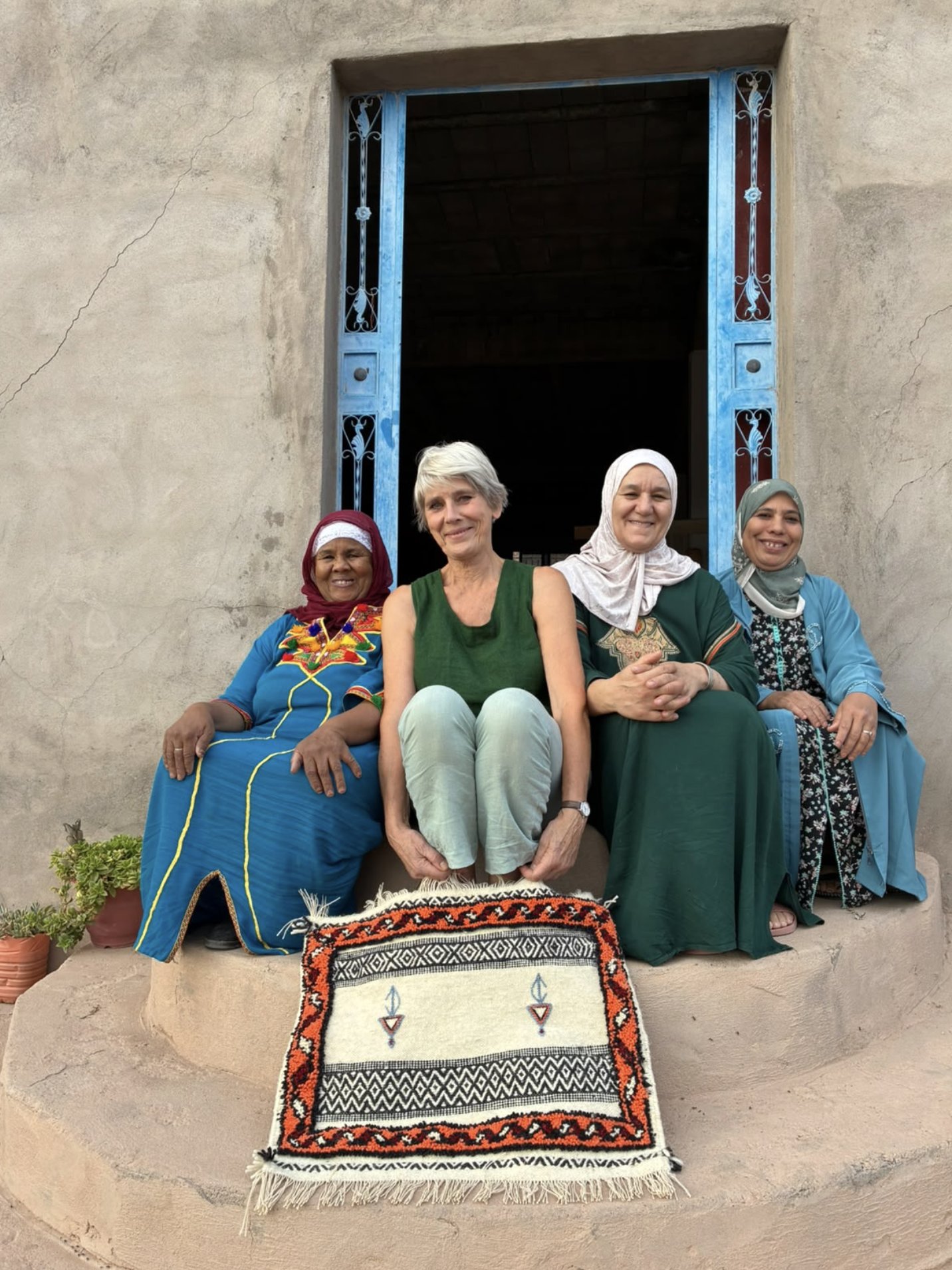 Mieke with three women of Cooperative Afous GAfous on the steps of a home in Lamdint, with her finished Glaoui rug at their feet