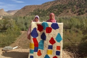 Two weavers holding up a finished rug