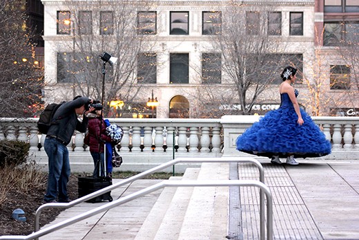 A girl twirls, posing for a photo to commemorate her quinceañera; Air Jordans peak out from below her ball gown. The stark contrast between shoes and dress mirrors the dichotomy between girl and city. Tradition holds on even as commerciality threatens to overwhelm it.