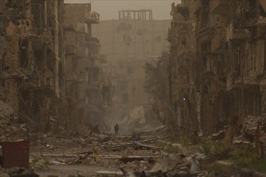  child walks past damaged buildings in Deir al-Zor, Syria