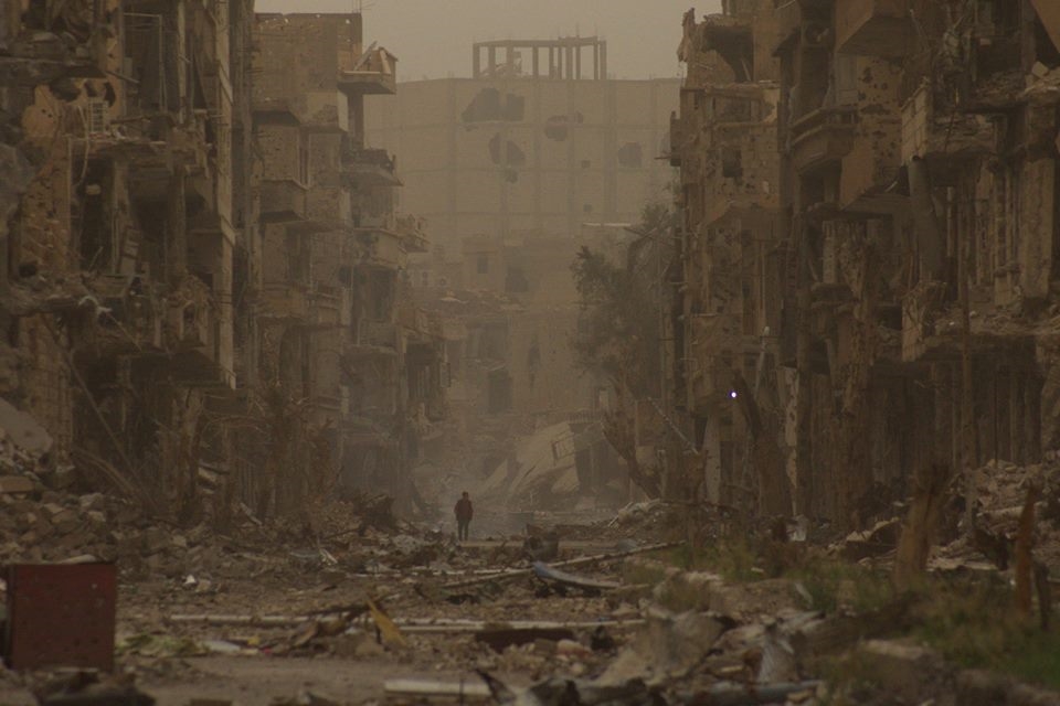  child walks past damaged buildings in Deir al-Zor, Syria