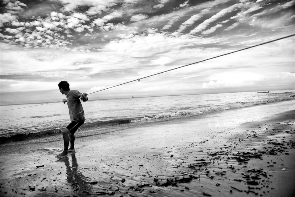 6h00: Traditional fisherman holding and pulling a net rope while his partners surround a big portion of water with their net on their boat.