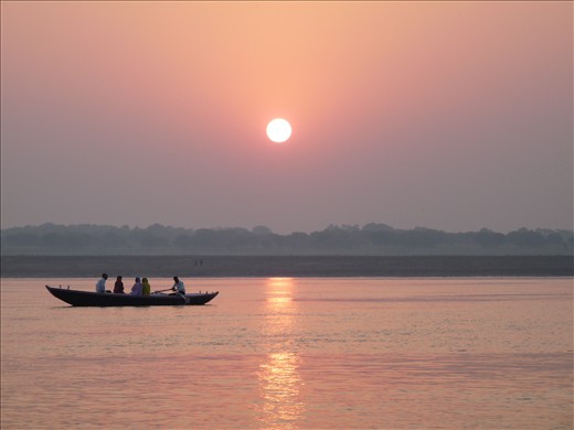 It is sunrise on the banks of the Ganges River in Varanasi, India. Rays of light push through the hot, heavy fog as people make their way to the sacred river for morning prayer. 