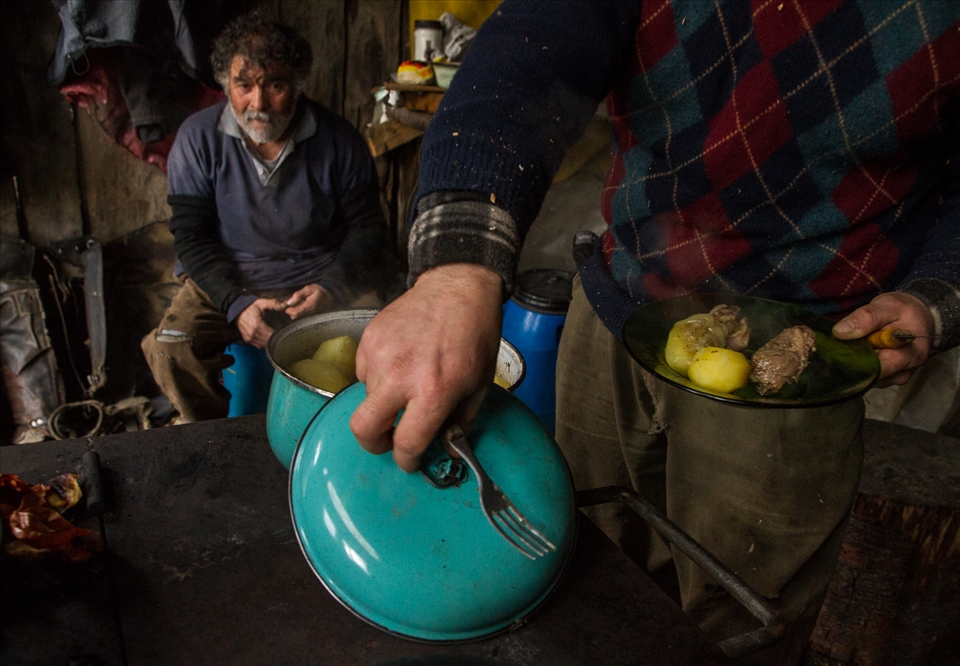 Meat and potatoes, a Patagonia staple of ranch life seen here on a plate, juxtaposed between the colorful lid of an old pot and the ranch laborers about to eat lunch.