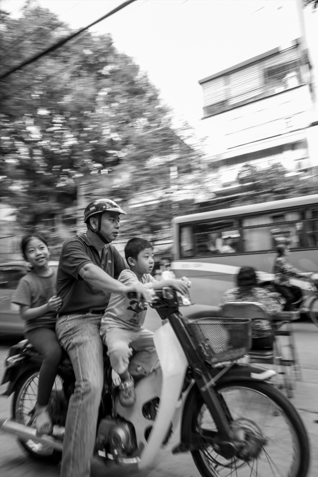 A man and his two children zip thru on scooter during rush hour. 