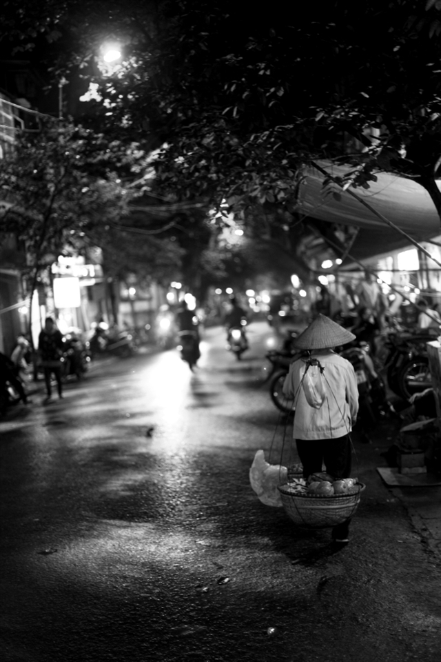 A street merchant wanders the city at night looking for sale. 