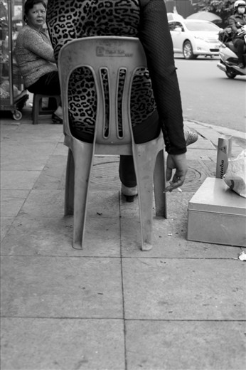 Lady sitting on the curb smoking a cigarette and watching life go by in Hanoi