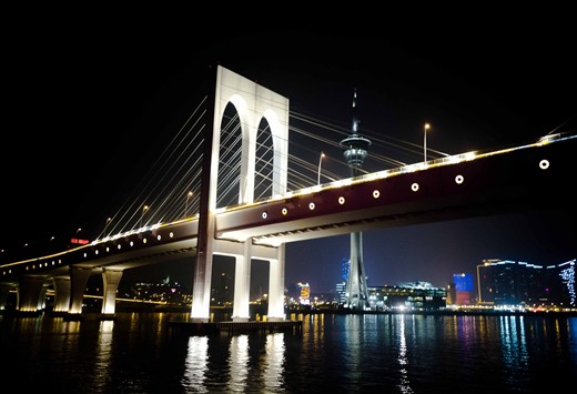 Macau, China - The lights of the Macau Bridge cuts thru the darkness a few hours before the start of the New Year. The Macau Tower can be seen behind it.