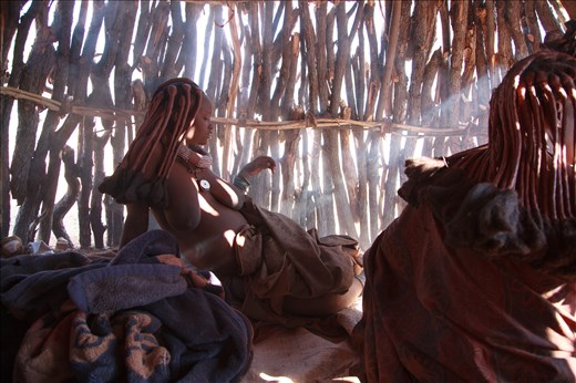 Menjamwapi sitting inside her self built hut during early phases of labor. In preparation for delivery she has built a mud hut with her sister. She would walk one hour daily with buckets of Mud and animal manure which were then used to construct the shelter. She gave birth before the hut was fully built.