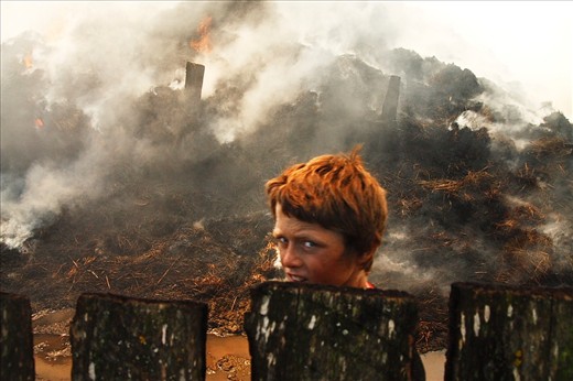 Constantin Puscaru passes by haystacks on fire in his neighbor's yard which are said to have caught fire from sparks thrown by a circular saw when building a new barn in Letea, Danube Delta, Romania.