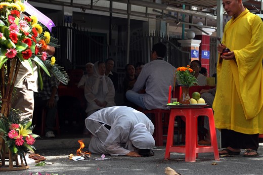 A woman dressed in the traditional white funeral clothes prays for her dead husband while a monk chants the compassion mantra needed. This wishes him a reincarnation close to the Buddha´s teachings and an existence without suffering. It is part of the rite to burn paper money and other needs for the last journey of the soul until next rebirth. 