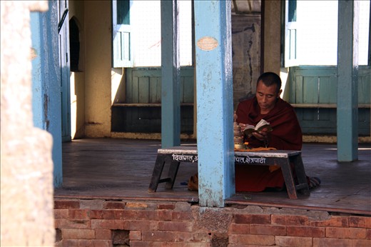 A buddhist monk sits quietly in chanted prayer amoungst the Stupa grounds.