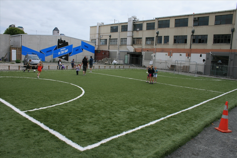 Football in the gap - local kids enjoy a new man-made soccer field near the city centre in the gap where a building used to stand between a pile of rubble from ruined shops and a cordoned off building with a questionable future.
