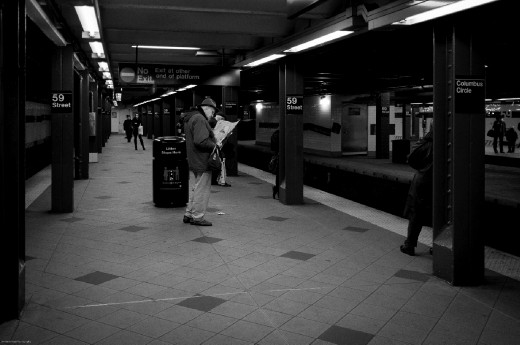 The Transit  Life of a New Yorker -
A man reads the paper while he waits for his train, even with all the commotion of trains whizzing by he stays affixed to the black and white tracks of text.