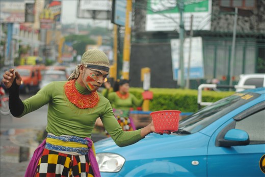 The dancer performed his dancing ability in front of vehicles that stopped by traffic light. They carried a basket to collect money from people.