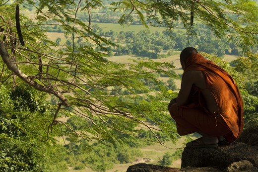 A monk perched peacefully on the edge of the mountain overlooking the Cambodian country side.
